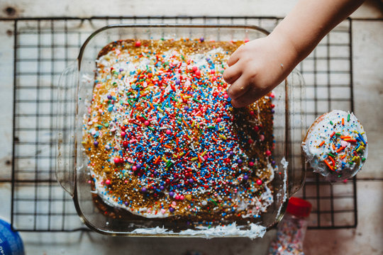 Young child stealing sprinkles off of freshly baked colorful cake