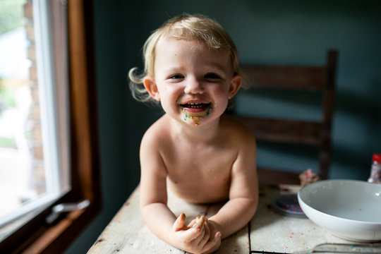 Toddler girl laughing with messy face after colorful sweet treat