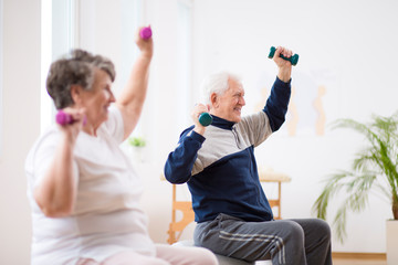 Elderly man exercising with his friend during pilates for seniors