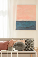 Grey and pastel pink pillows on trendy Scandinavian couch in elegant interior with painting on the white wall