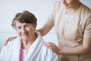 Obraz premium Redhead pretty nurse in beige uniform with her hands on senior woman shoulders