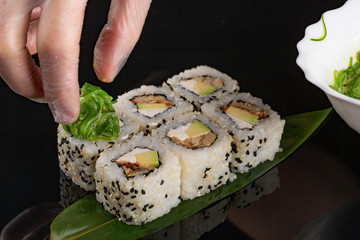 Decoration with seaweed. Close-up of a cook hands putting seaweed on tuna sushi rolls
