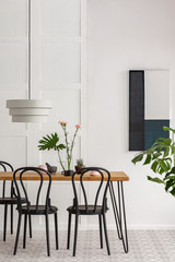 White lamp above wooden table with black chairs