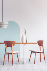White lamp above long wooden table with vases and stylish chairs