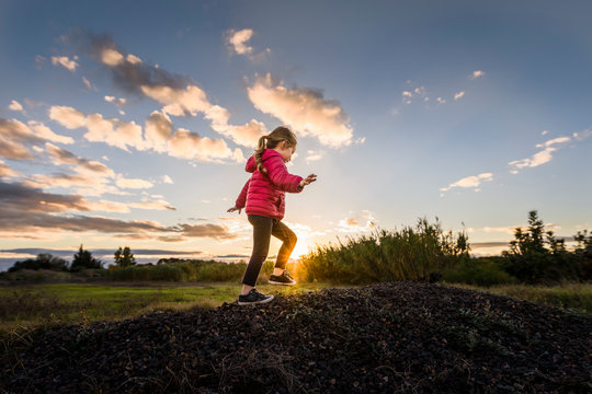 Child climbs pile of stones at sunset with sunburst and cloudy sky