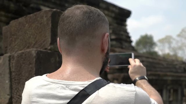 Tourist standing in old ruins and doing photos on smartphone