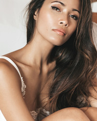 close up of a gorgeous and sexy Filipino model with long curly hair and in white lingerie sitting...