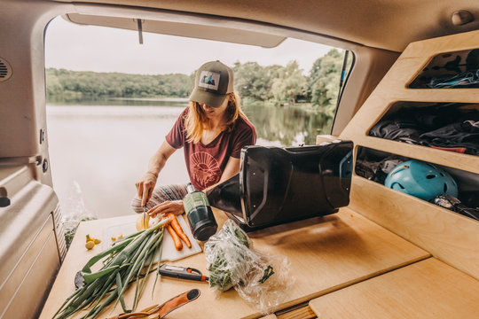Woman cuts vegetables in back of built out van by a lake in RI