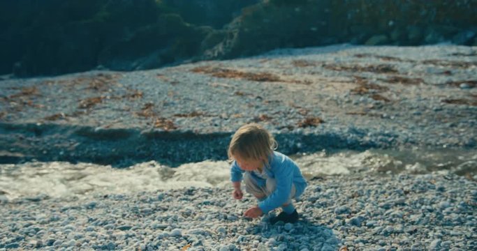 Little toddler picking up rocks and throwing them in stream on beach