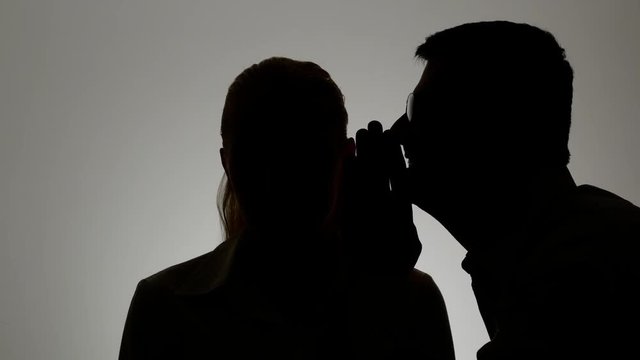 Silhouette of a man and a woman. A man whispers in a woman's ear.
