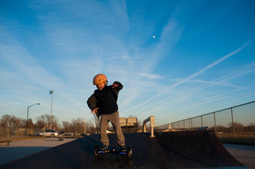Young boy riding down ramp at skatepark against blue sky