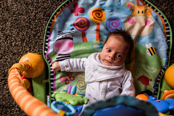young baby laying on play mat looking up at toys hanging down