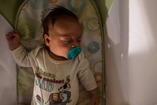sleeping baby in a bassinet with pacifier and sunlight on face