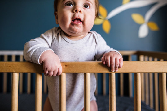 close up of drooling baby standing and leaning against crib rail