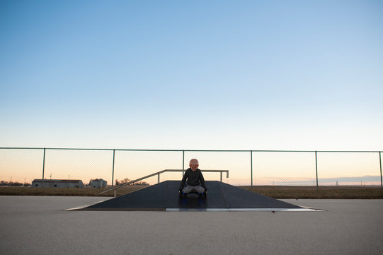Centered image of boy comping down ramp at skate park on knees