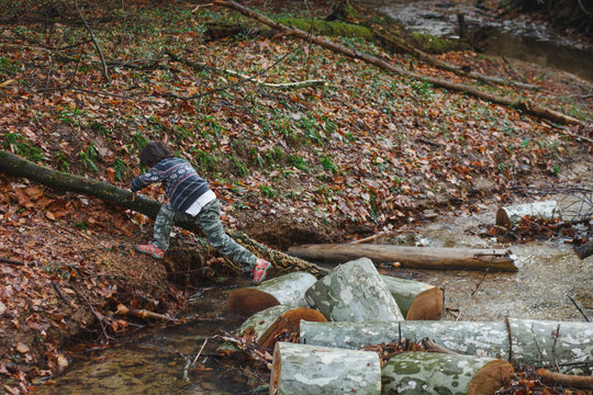 A small child plays and jumps in a creek in the woods - Powered by Adobe