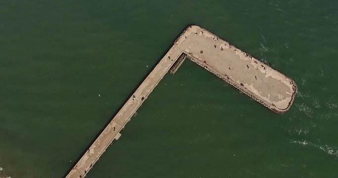 Orbit around pier jetty in San Francisco, California. Spinning to reveal the shore. People walking on the pier on a bright day. People fishing.