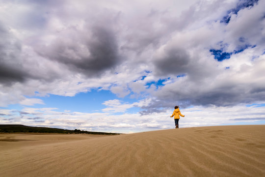 Girl runs along sand dunes at beach under big sky with clouds France