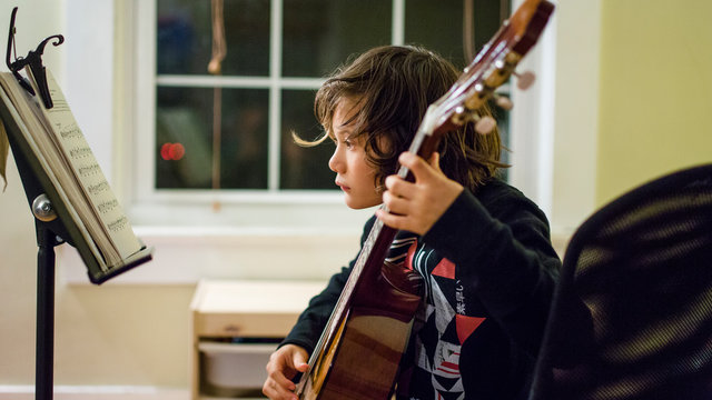 a young boy reads music and practices guitar