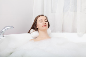 Obraz na płótnie Canvas Young pretty woman relaxes in bathtube with soap foam. Spa procedures in bathroom at home or hotelroom. Skin care and moisturizing for youth preservation.