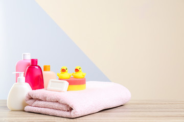 Baby cosmetic products, toys and towel on table against color background. Space for text