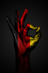 A hand with the painted flag of Germany shows an OK sign on a dark background.