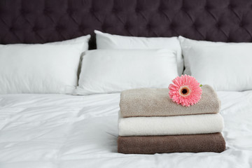Stack of clean towels and beautiful gerbera flower on bed. Space for text