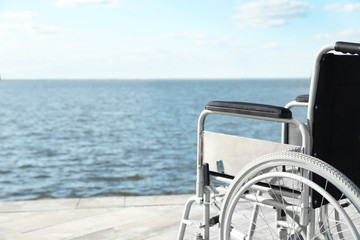Empty wheelchair near river on sunny day. Space for text