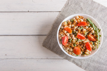 Vegetarian salad of boiled chickpeas, cheese, arugula, mustard and cherry tomatoes on white wooden background.