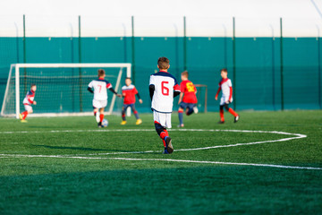 Boys at white red sportswear run, dribble, attack on football field. Young Soccer players with ball on green grass. Training, football, active lifestyle for kids  