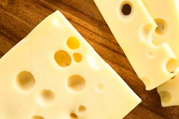 Piece and slices of Emmental, Emmentaler or Emmenthal cheese, photographed overhead on wood