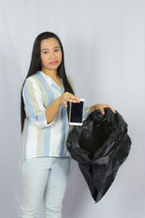 Woman throwing her phone into the garbage bag, posing isolated on gray background.
