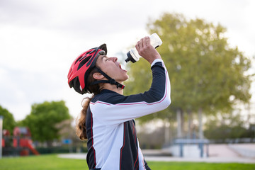 From below side view of young thirsty fit male cyclist in sportswear and protective helmet drinking...
