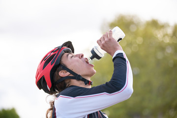 Naklejka premium Young tired cyclist drinking water in park