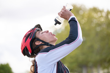 From below side view of young thirsty fit male cyclist in sportswear and protective helmet drinking...
