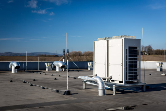 Air vents on the roof of building in functional and operational condition. Around are seen vent pipes and lightning rods. Sky is blue and the background is slightly blurred, focus on ventilation unit.