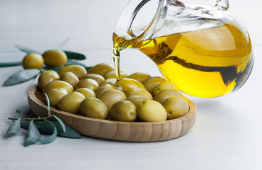 Pouring homemade olive oil from bottle into glass on raw turkish green olives in bamboo bowl,...