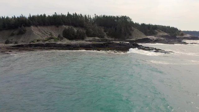 Cinematic drone / aerial footage rotating showing a bay, someone taking pictures on the rocks and a dog in the cost of Kingsburg, Nova Scotia, Canada during summer season.
