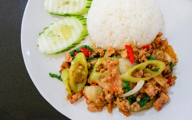hot and spicy stir fried holy basil minced pork and fried egg on cooking rice on plate with cucumber