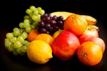 Beautiful juicy fruits on a black background: apples, grapes, oranges, bananas, close-up