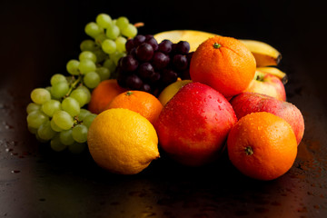 Beautiful juicy fruits on a black wet background: apples, grapes, oranges, bananas, copy space, close-up
