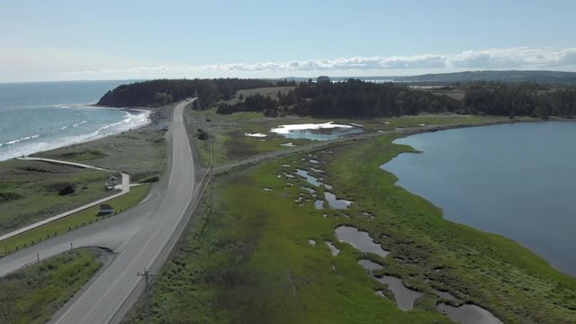Cinematic drone / aerial footage rotating showing a road by the ocean and waves hitting the beach at Cole Harbour coast in Lawrencetown, Nova Scotia, Canada during summer season.
