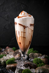 Milkshake. Cold drink of milk, ice cream, chocolate and caramel on a black background with stones and ice. Cocktail card for a bar or restaurant.