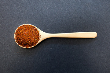 Red chilli powder on wood spoon, top view spices on black background isolated.