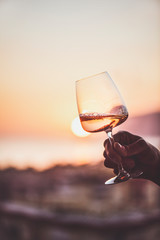 Glass of rose wine in man's hand with sea view and sunset at background, close-up. Summer evening relaxed mood concept - 264066939