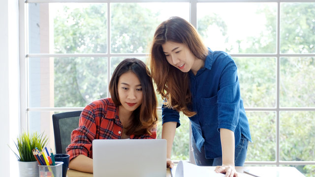  Two young asian women working with laptop computer at home office with happy emotion, working at home, small business, office casual lifestyle concept