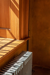 Fototapeta na wymiar Bright light from a window streaming across a warm wood windowsill and vintage metal radiator, vertical aspect