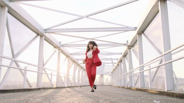Happy beautiful afro-american woman walking and dancing outdoor. Young mixed race carefree girl enjoys the day and dancing in slow motion. Black lady walking on pedestrian walkway. Steadicam shot.