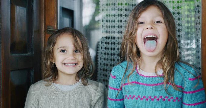 Authentic shot of two cute little girls showing coloured tongue after lollipop and smiling in camera outside her house on a sunny day.