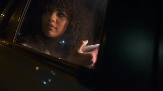 Beautiful Afro American woman tourist traveling in a taxi and rewritten with your friends on your phone at night.  Passenger Girl looking at cellphone at night in the back seat of a car.